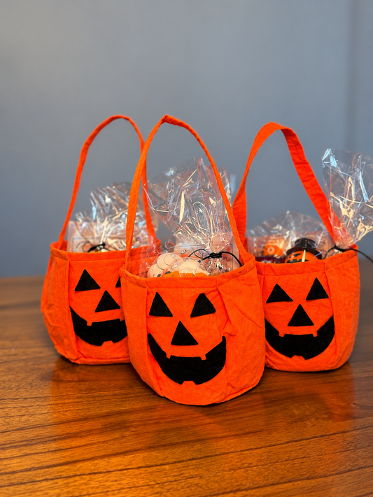 Three orange jack-o'-lantern bags holding wrapped Halloween goodies